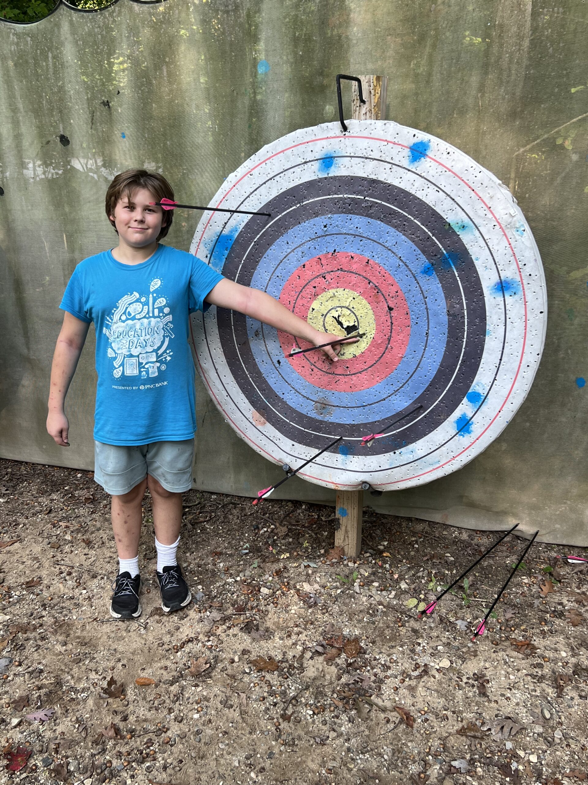 A young boy stands in front of an archery target showing off wear his arrows struck. TrueMentors. student mentee