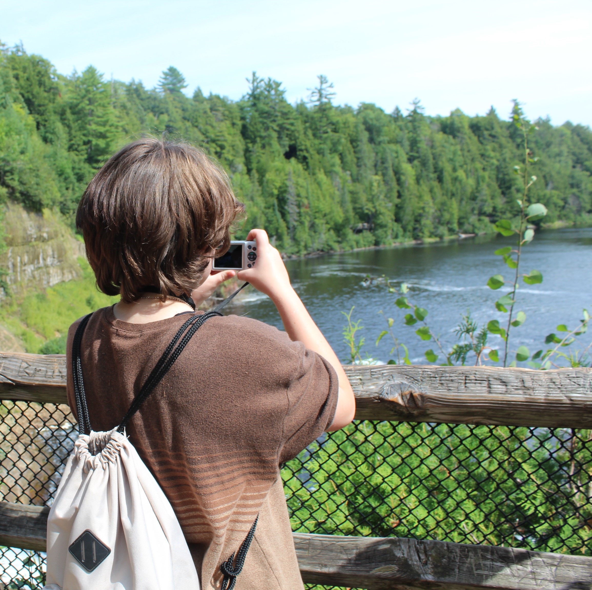 Student named Danny holding a camera in front of him taking a picture of a river, at Parks in Focus. TrueMentors