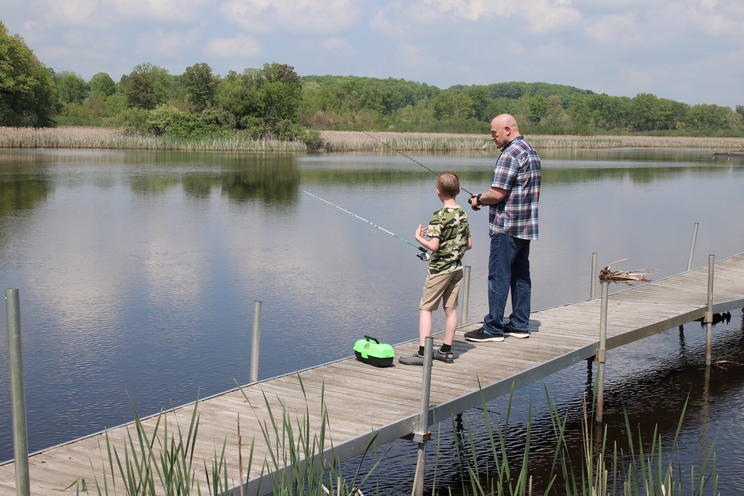 An adult male mentor and young male mentee standing on a dock fishing