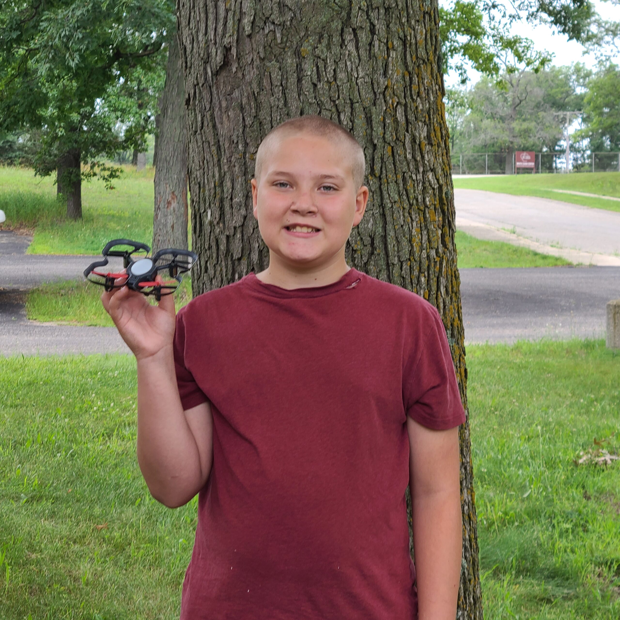 Middle-school aged boy named Trevor wearing a red t-shirt,, holding a drone outside