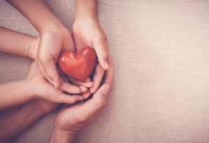 Multiple hands holding a heart representing Giving Tuesday.