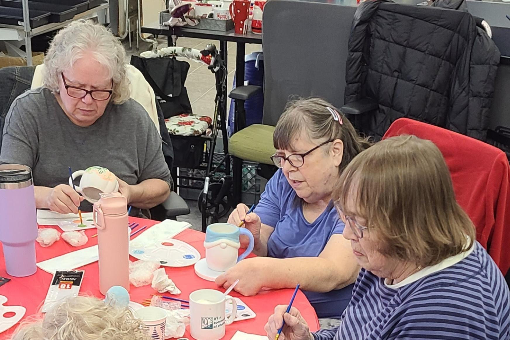 Three senior women working on decorating pottery at a table.