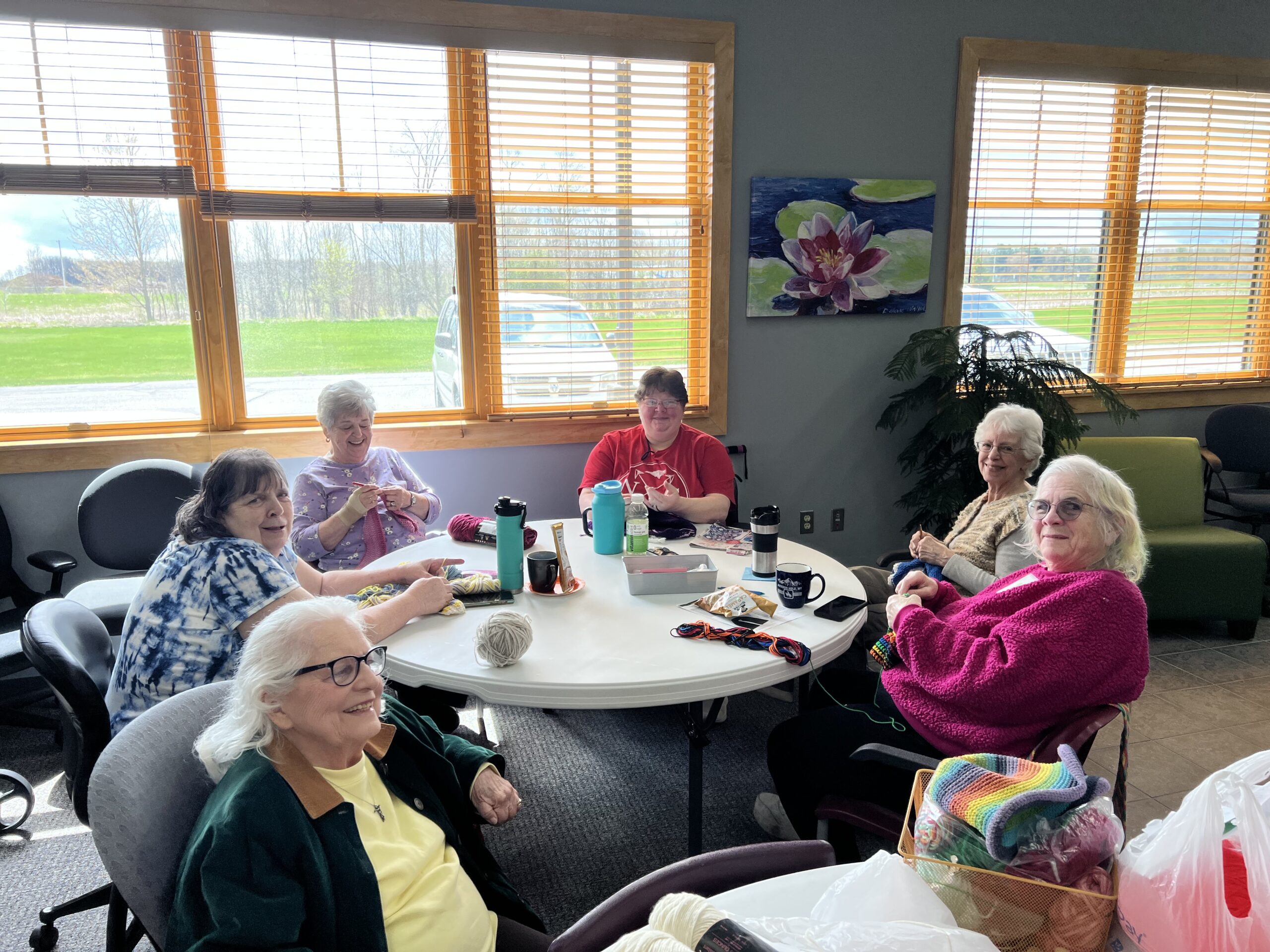 Group of six ladies sitting around a table knitting.