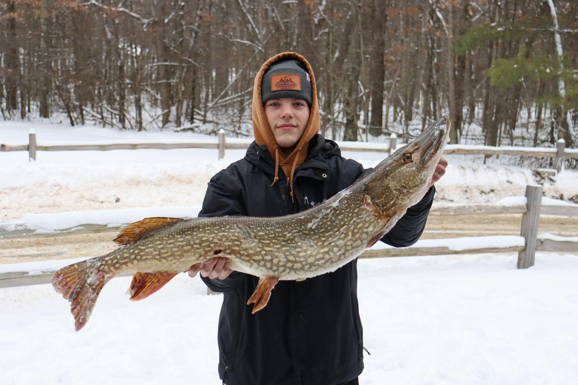 Male teenager outside in the snow, holding a larke pike he caught ice fishing at the Dam to Dam ice fishing tournament