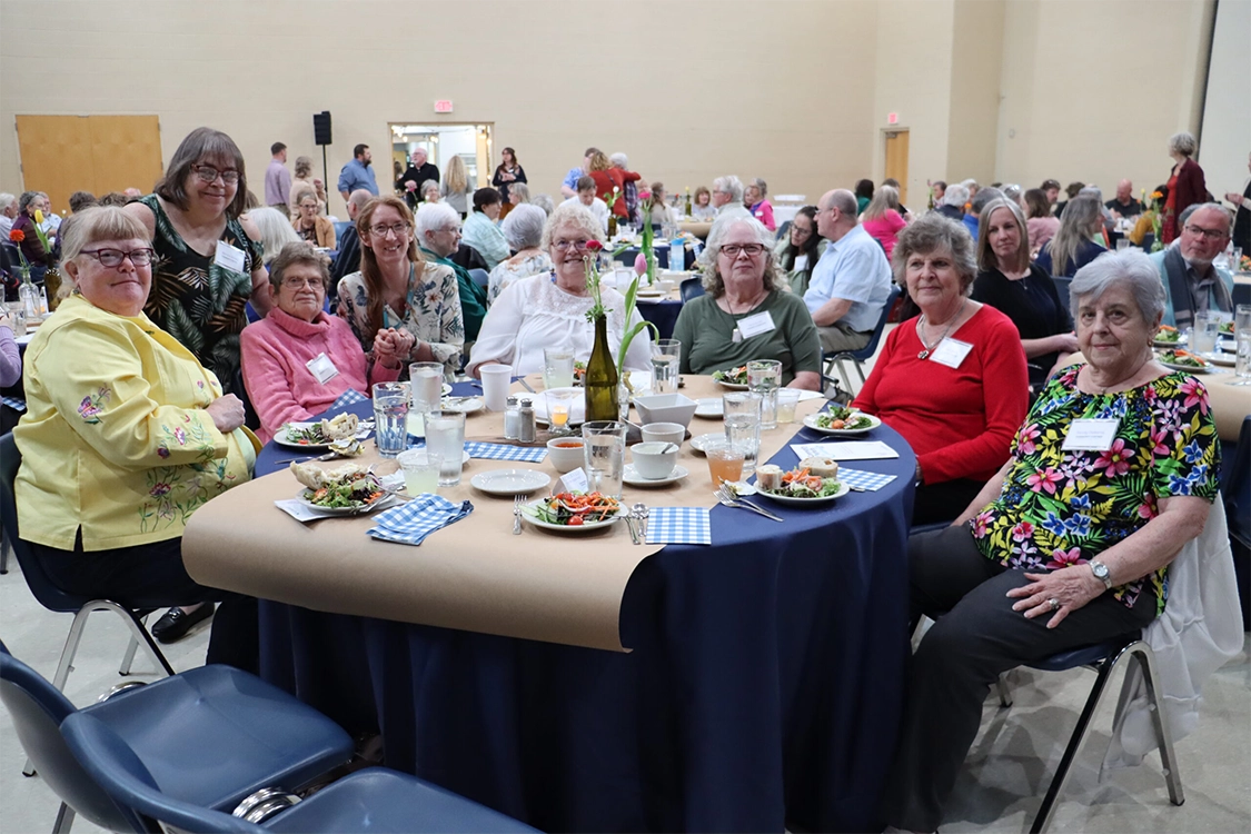 7 older women around a table at the Community of Efforts event with Community Connections staff member Christa Smalligan