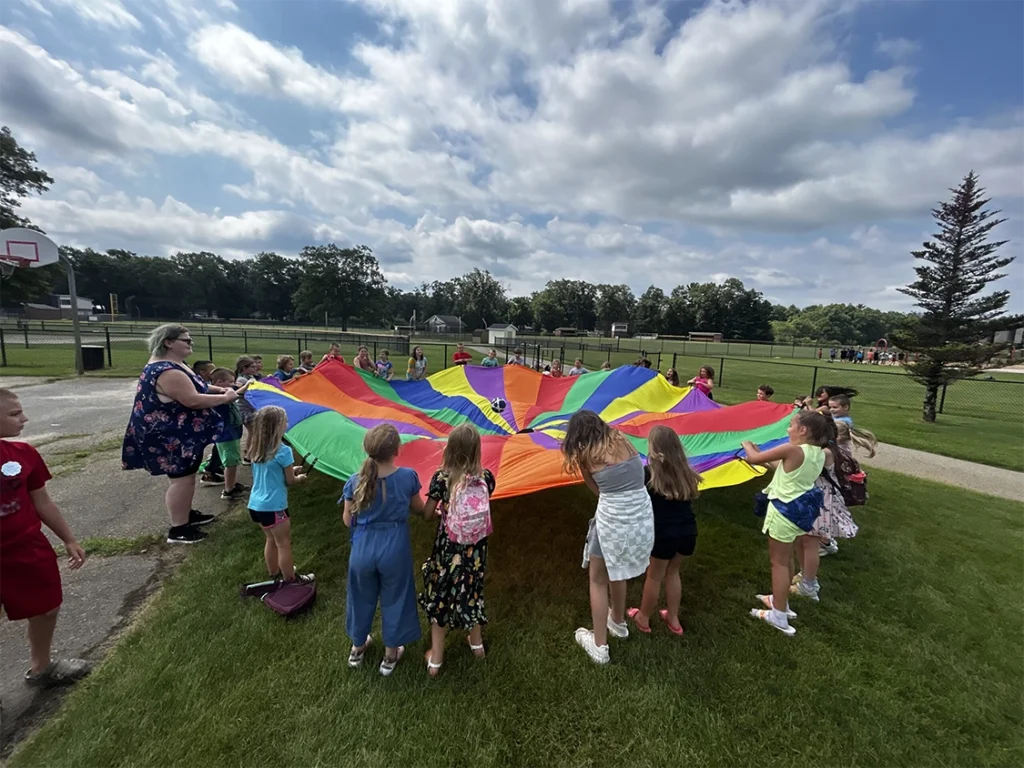 group of elementary kids playing with a rainbow colored parachute