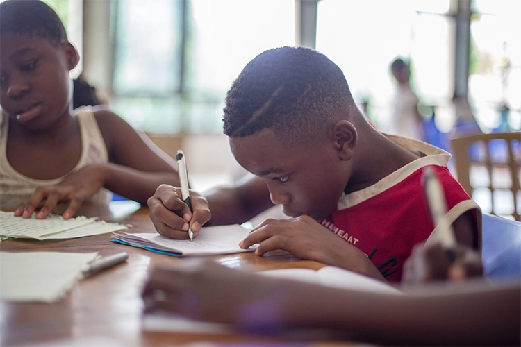 Elementary boy doing homework at a table with other children.