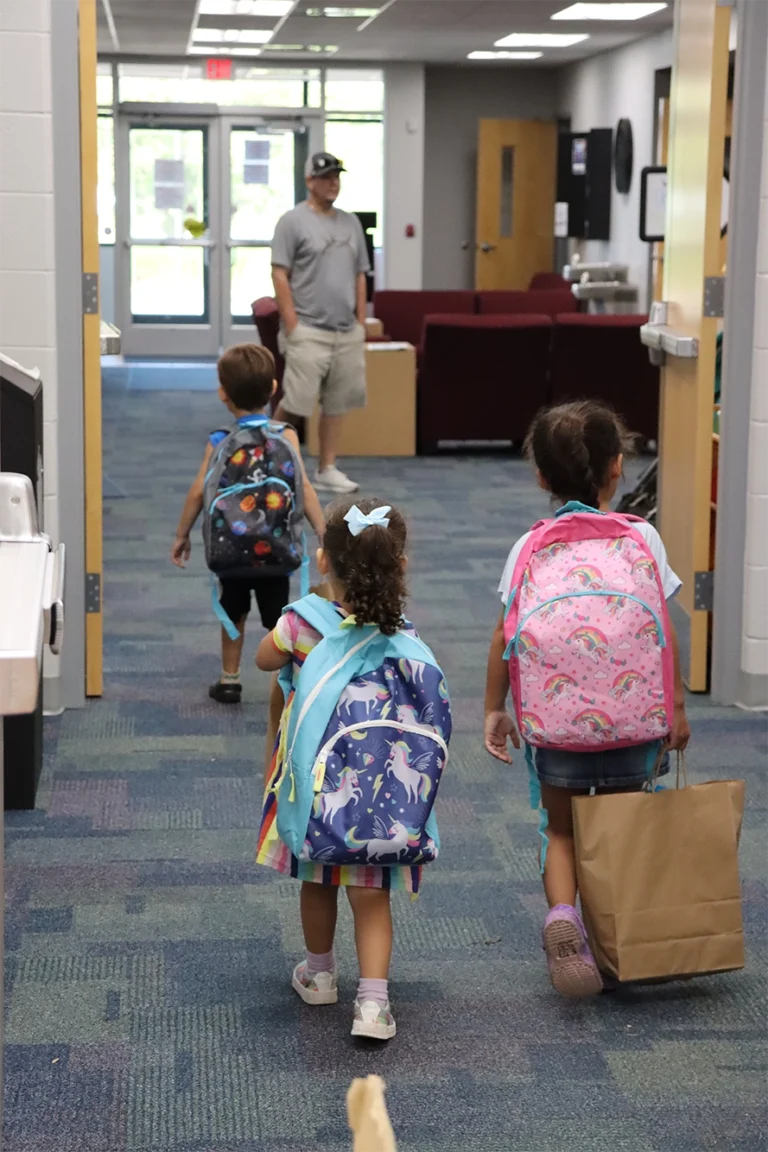 Three children with backpacks walking away with their new school supplies