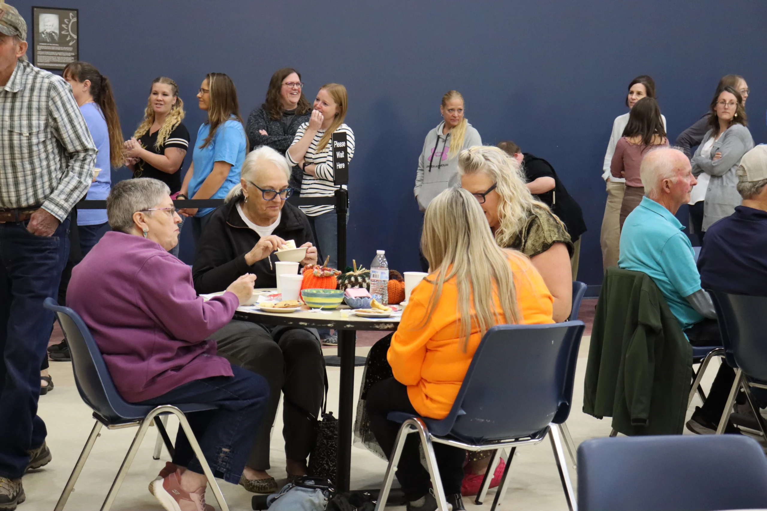 Four women at a table enjoying soup at Empty Bowls, while several more people wait in line behind them.