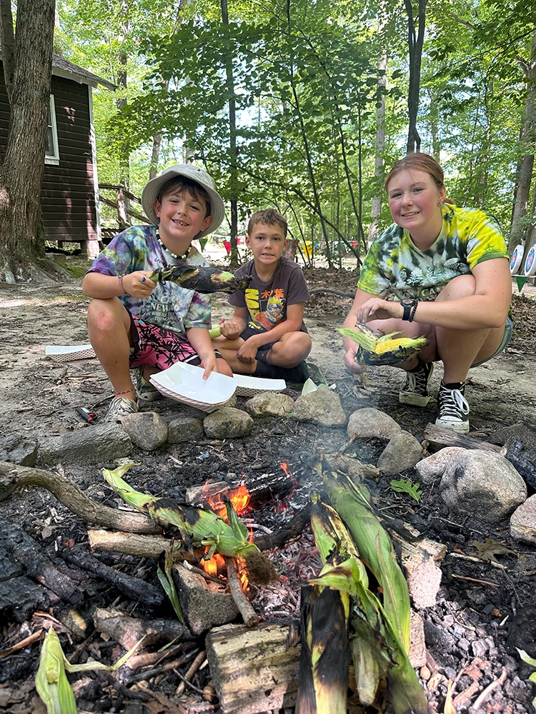 campers roasting corn on the cob over an open fire