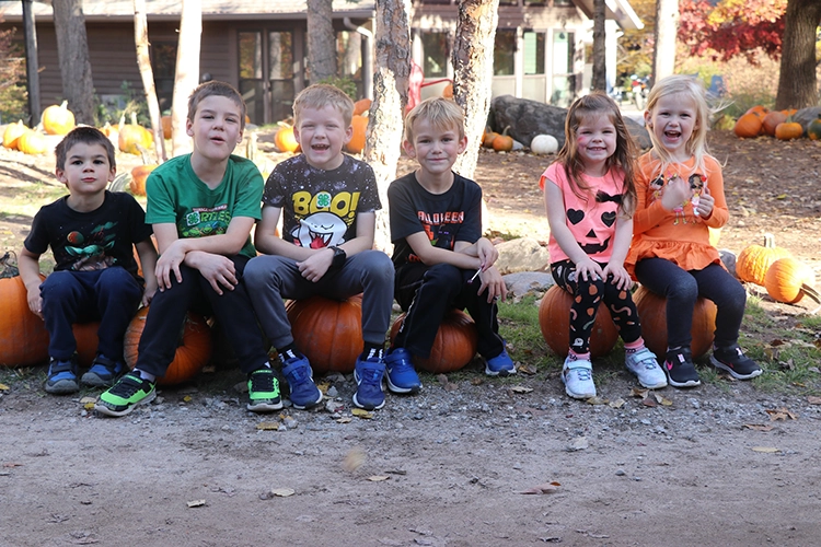 Children sitting on pumpkins while smiling