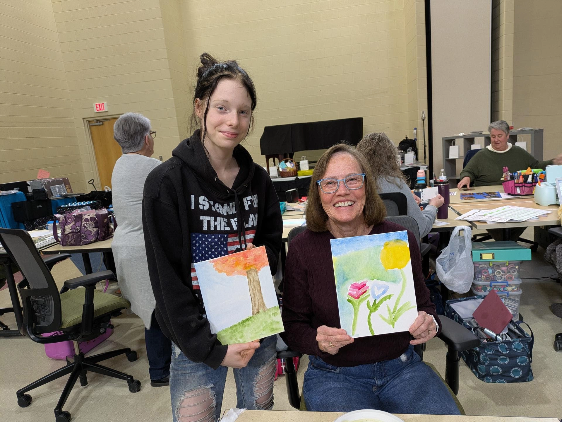 A young teenage girl on the left next to her adult female mentor on the right, both holding artwork they created.