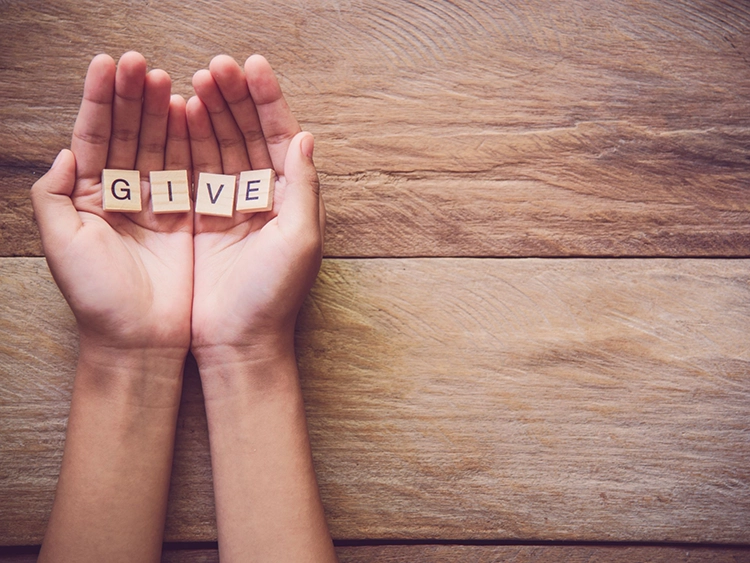 Hands holding the wooden letters that spell out the word give.