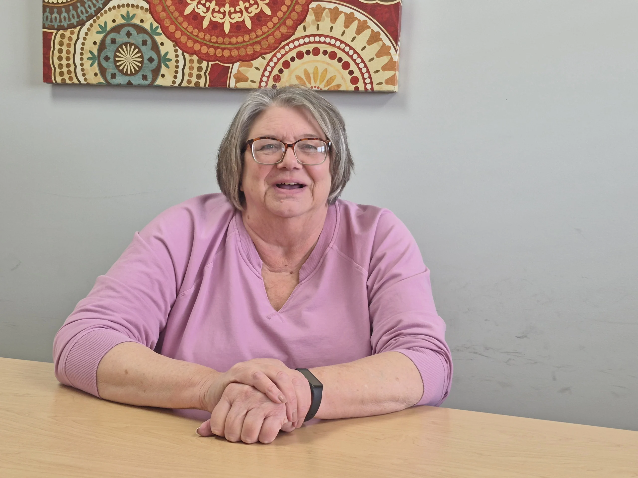 An older woman in a pink shirt at a table